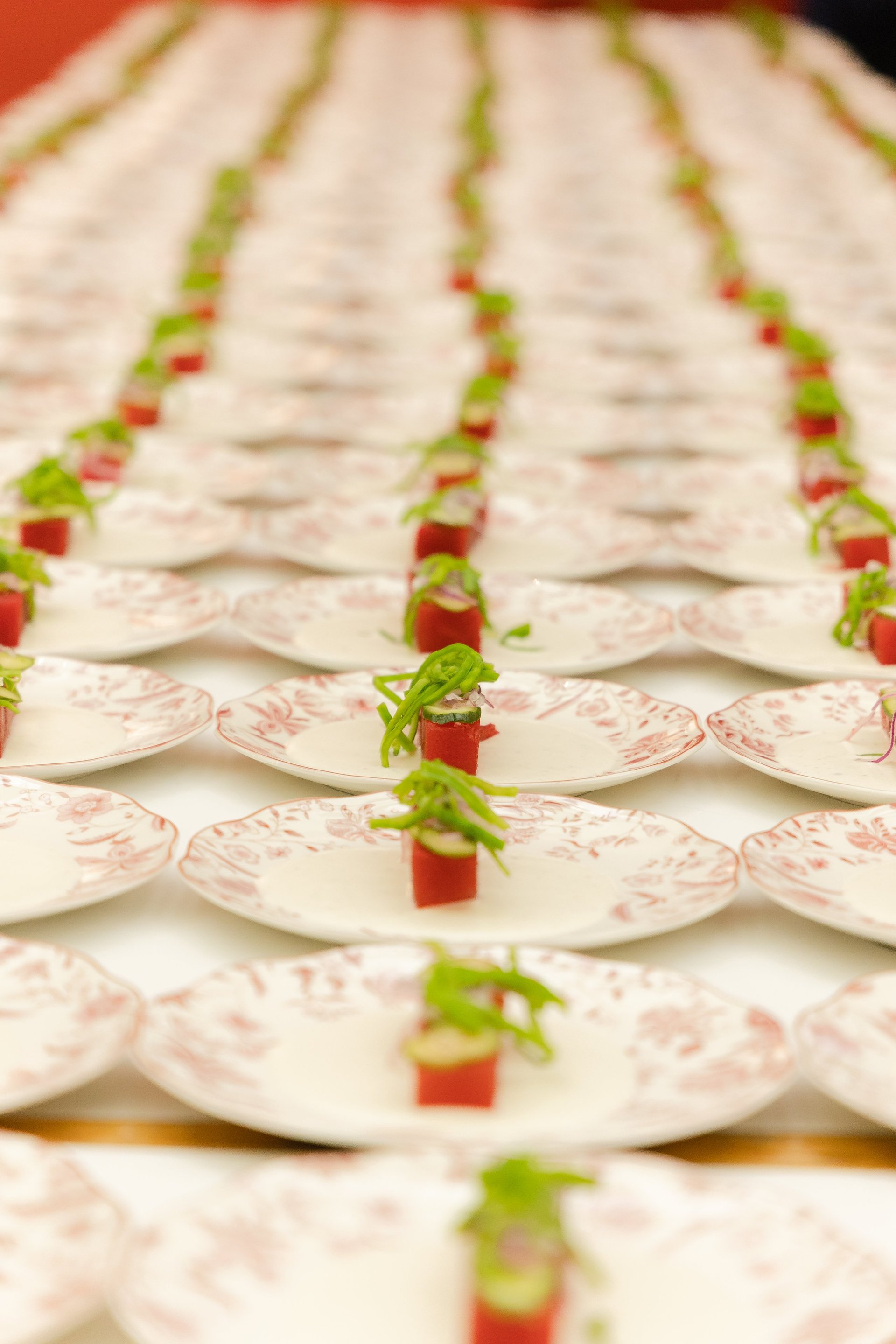 Rows of plated appetizers with cream-colored ceramic dishes, each garnished with red diced vegetables and green microgreens