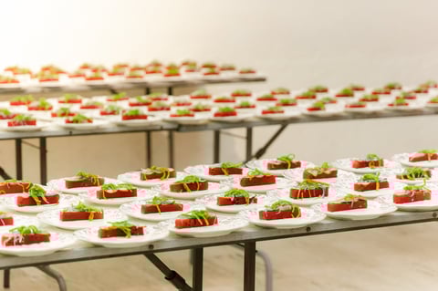 Multiple rows of catered appetizers on long tables, each featuring tomato, lettuce, and sauce on bread